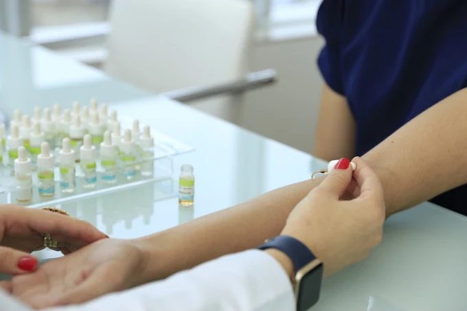 Prick teste sendo aplicado no antebraço de uma paciente, com os frascos de alérgenos na mesa